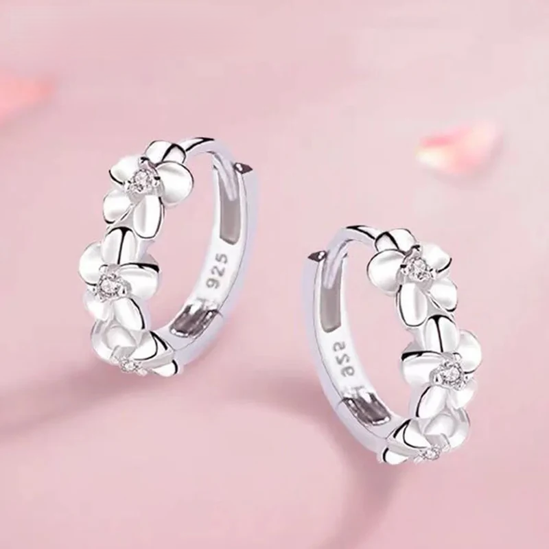 Silver hoop earrings with floral designs on a pink background