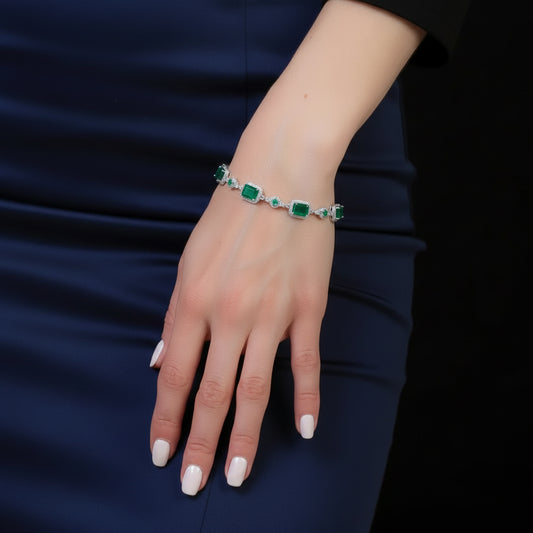 A silver-toned bracelet with rectangular green emerald-cut stones, worn on a woman's wrist. The image shows the model's hand and arm resting against a dark navy blue dress, with a solid black background on the right.