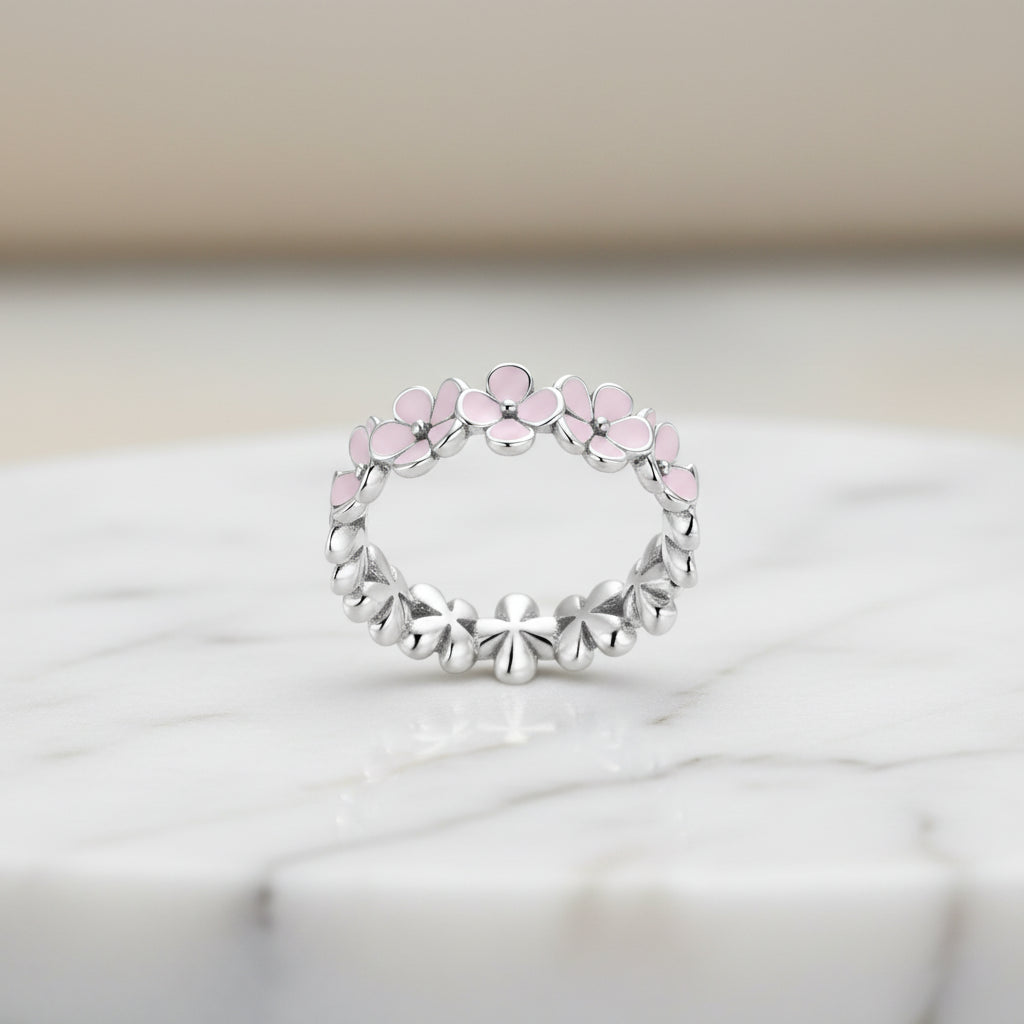 A silver ring with pink accents, featuring a floral pattern in a twisted metal design.