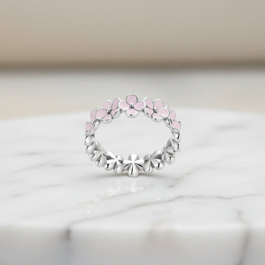 A silver ring with pink accents, featuring a floral pattern in a twisted metal design.