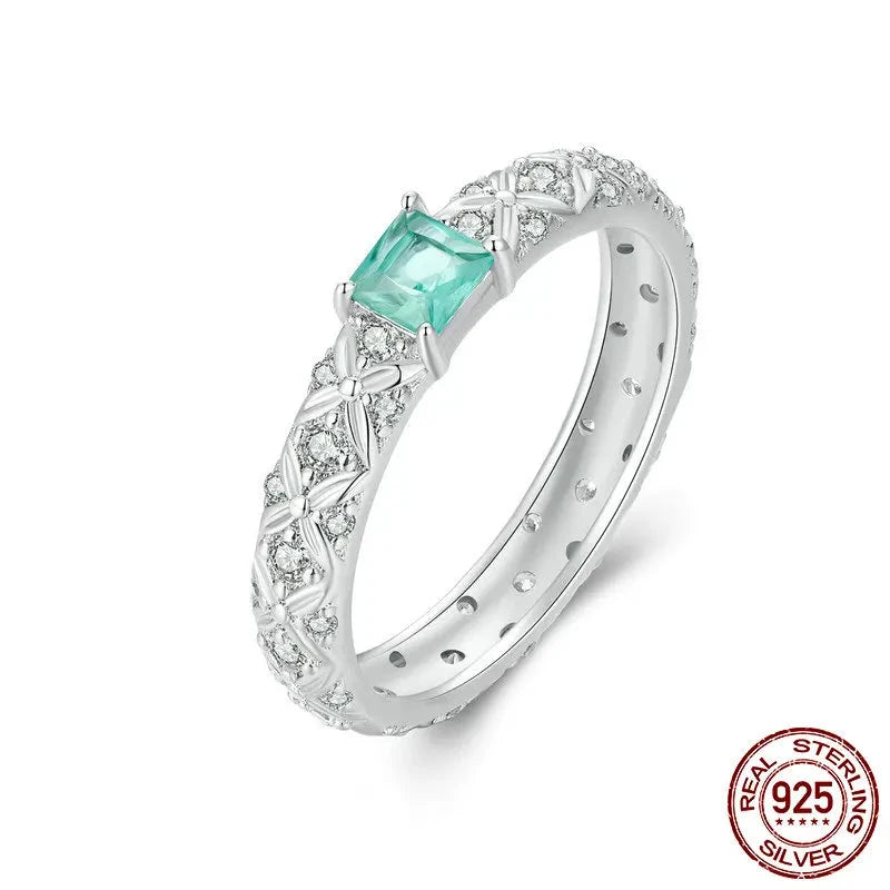 A 925 sterling silver ring with a central cubic zirconia stone, surrounded by small clear stones set in a geometric pattern, with a textured band and a small diamond-like stone on the top.