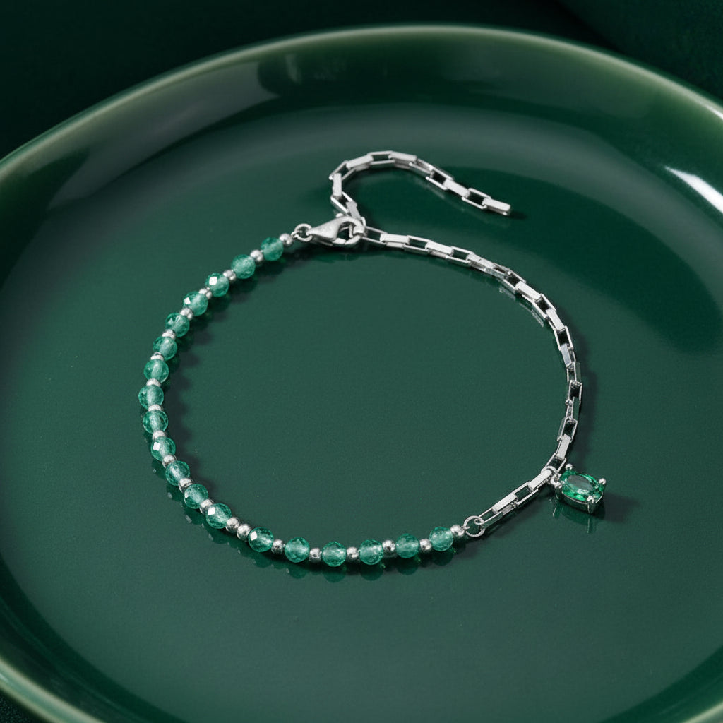 A silver-toned bracelet with faceted green beads and a small green rectangular accent stone, displayed on a dark green textured background.