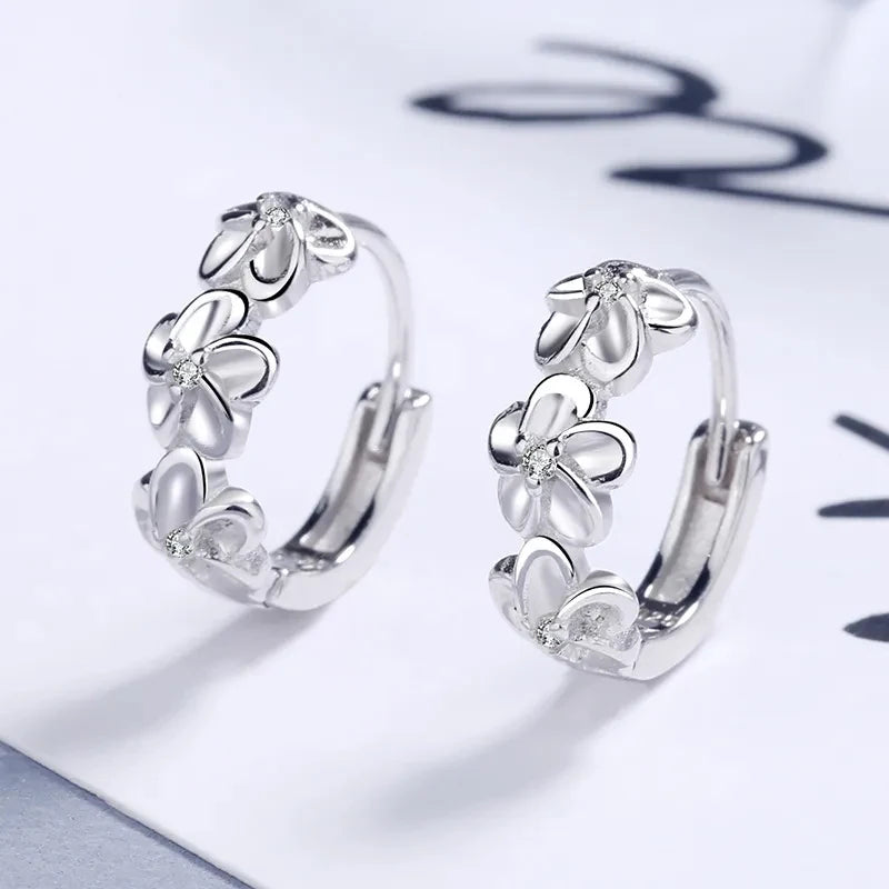 Silver hoop earrings with floral designs on a white surface

