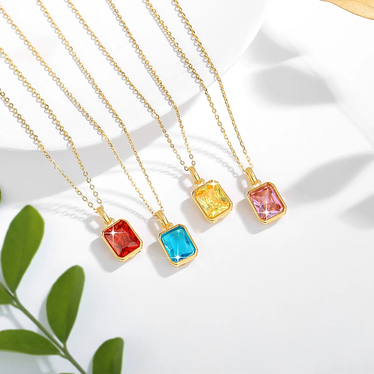 Four emerald-cut cubic zirconia pendant necklaces in red, blue, yellow, and pink set in elegant 18K gold-plated frames with matching gold chains