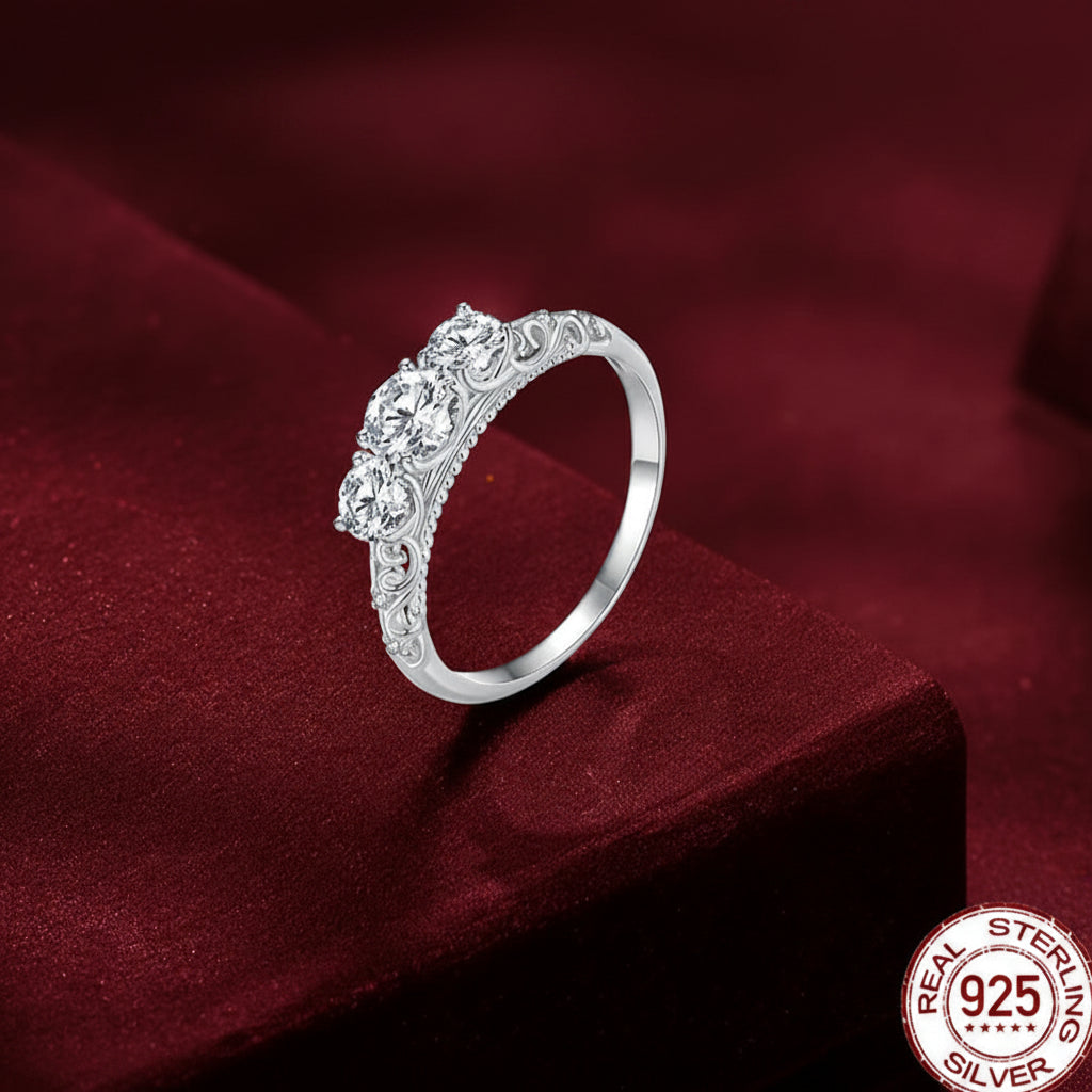 A silver ring with a decorative filigree band and a cluster of clear gemstones on the front, displayed on a deep red velvet surface. A '925 Sterling Silver' logo badge is visible in the bottom right corner.