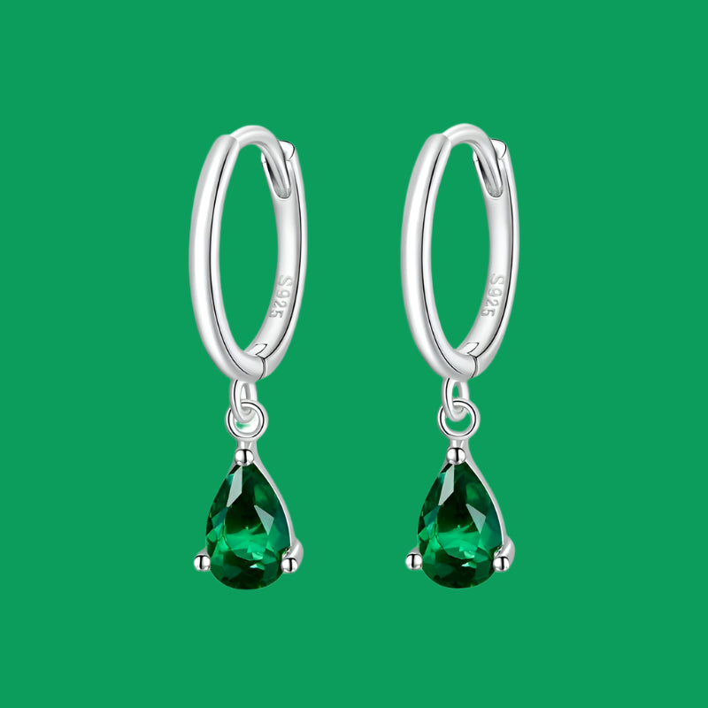 A pair of silver hoop earrings with green zircon stones attached to the hoops.
