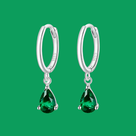 A pair of silver hoop earrings with green zircon stones attached to the hoops.
