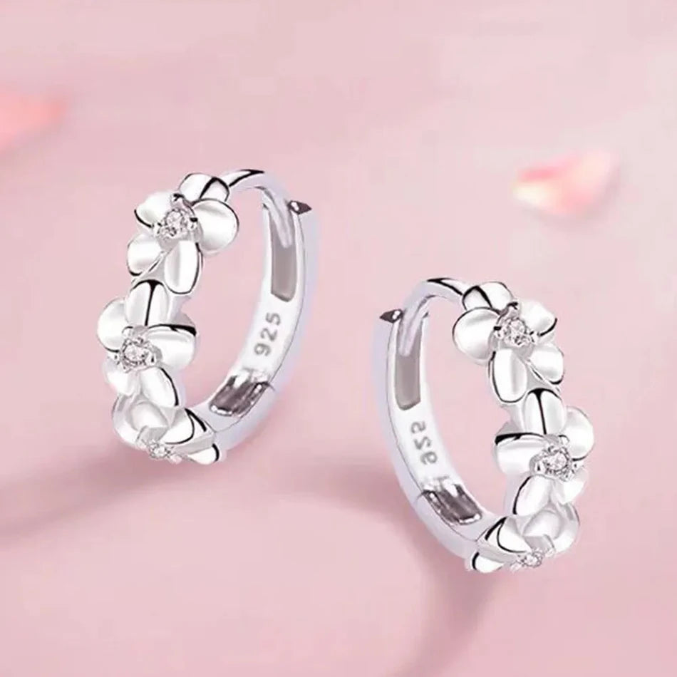 Silver hoop earrings with floral designs on a pink background
